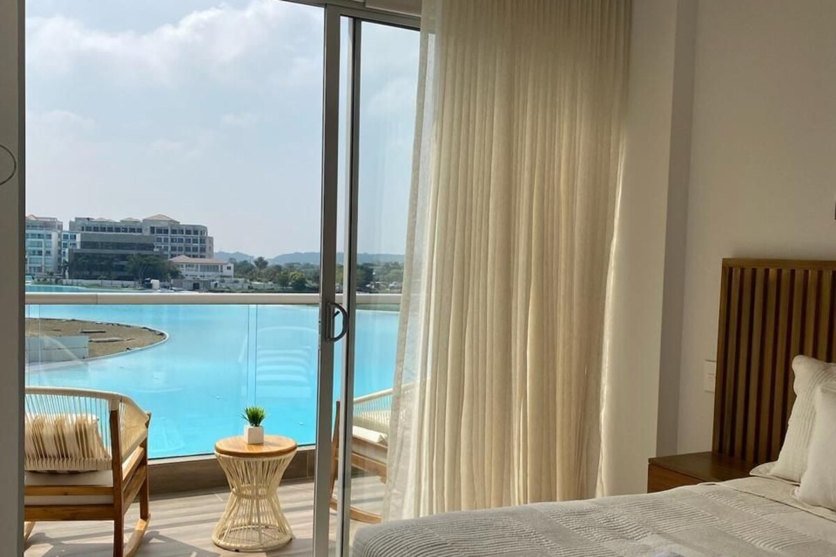 A hotel room with a large bed, a view of a pool, and a chair by the window.