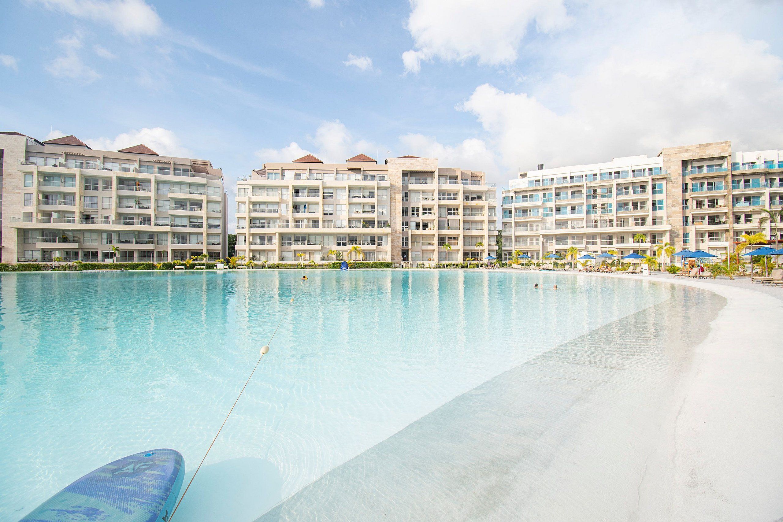 A large swimming pool with a clear blue water surface, surrounded by multi-story hotel buildings with balconies.