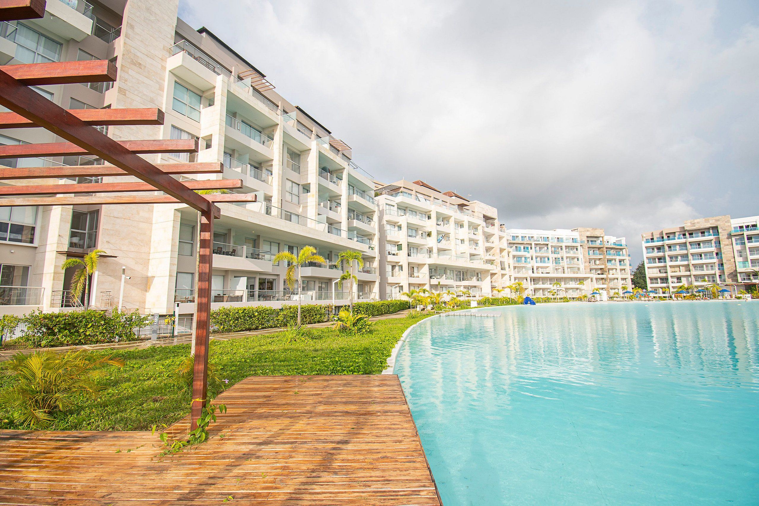 Un hotel moderno con una amplia piscina, varios balcones y abundante vegetación.