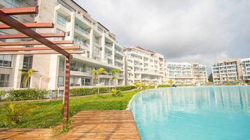 Un hotel moderno con una amplia piscina, varios balcones y abundante vegetación.