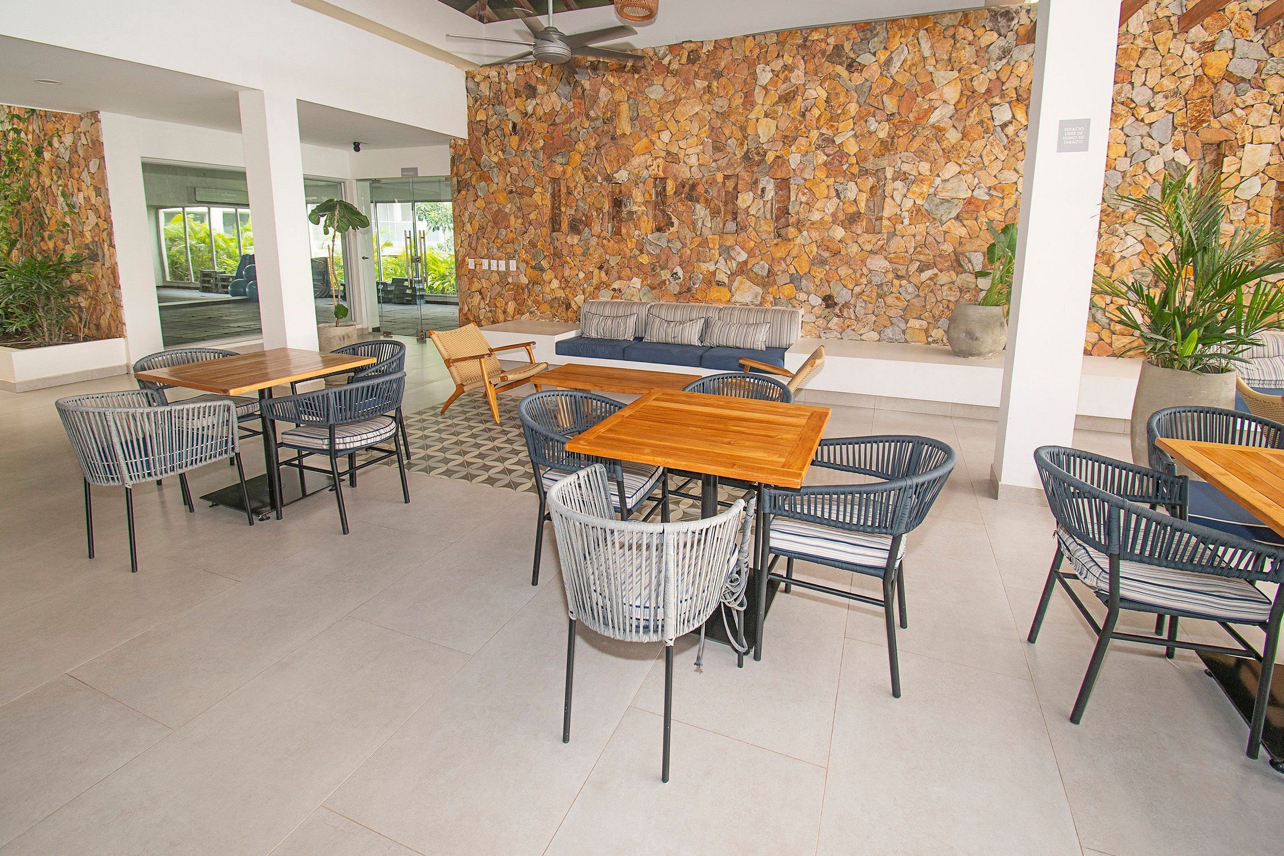 Un espacio interior amplio con pared de piedra, varios conjuntos de asientos que incluyen un sofá y sillas, y una mesa de madera.