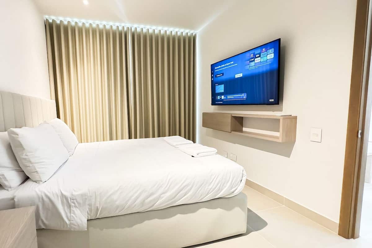A modern hotel room with a bed, a mounted TV, and a window with curtains.