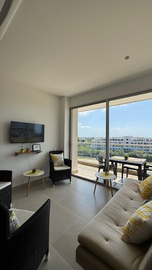 A spacious living area with a large window, a flat-screen TV, and comfortable seating.