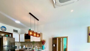 A modern kitchen with a central island, bar stools, and a dining area with a sofa and ottoman.