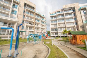 Un edificio residencial con varios balcones, un parque infantil y una pequeña estructura de madera.