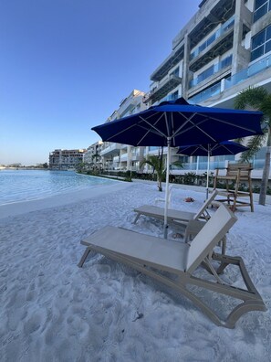 Un resort frente al mar con piscina, sillones de playa y sombrillas.
