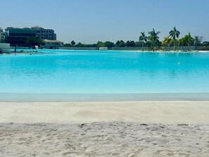 Una playa con piscina azul cristalina, orilla de arena y palmeras.