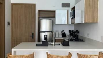 A modern kitchen with a central island, stainless steel appliances, and three wicker bar stools.