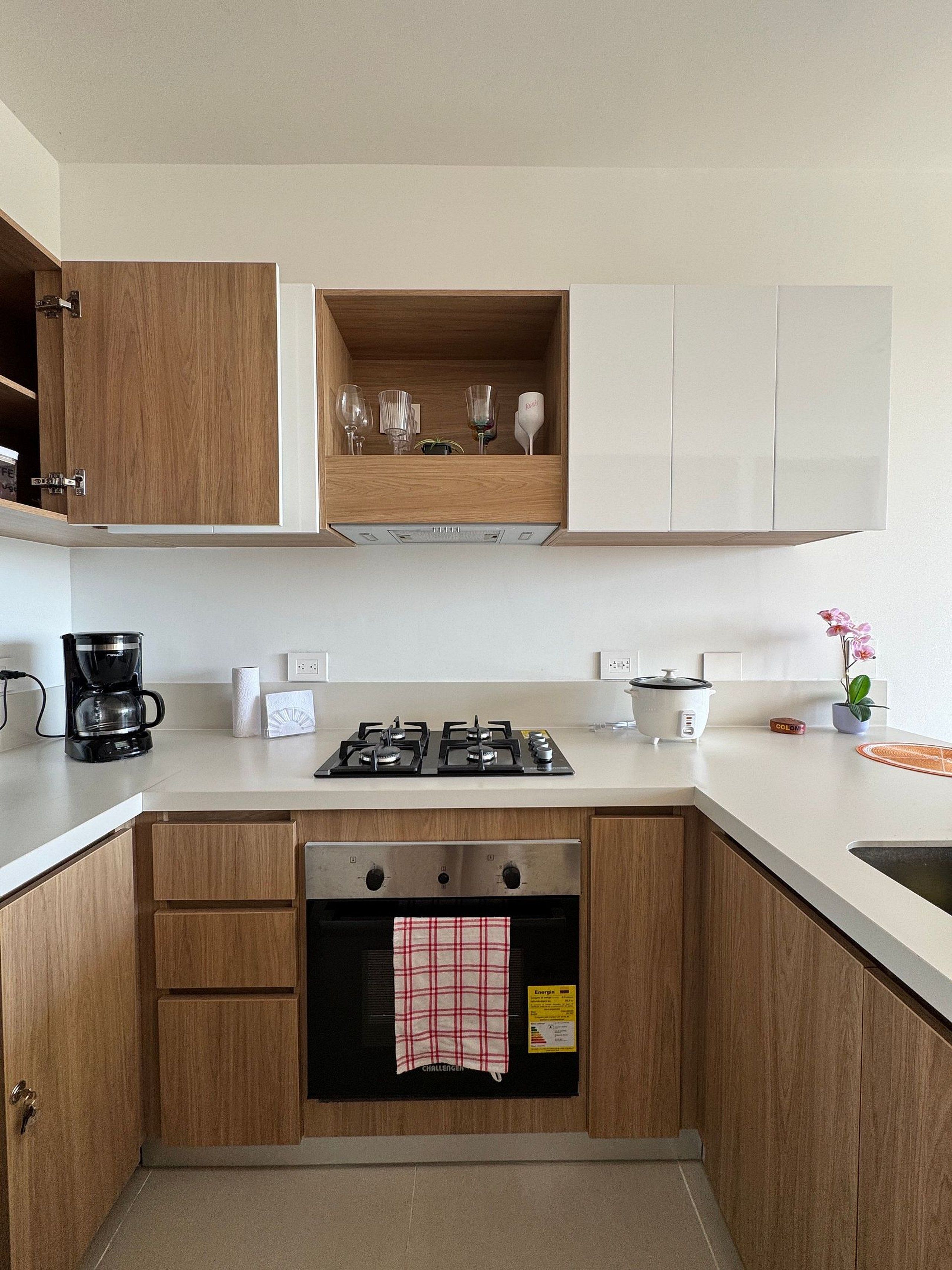Una cocina moderna con armarios de madera, horno empotrado, estufa a gas y cafetera.