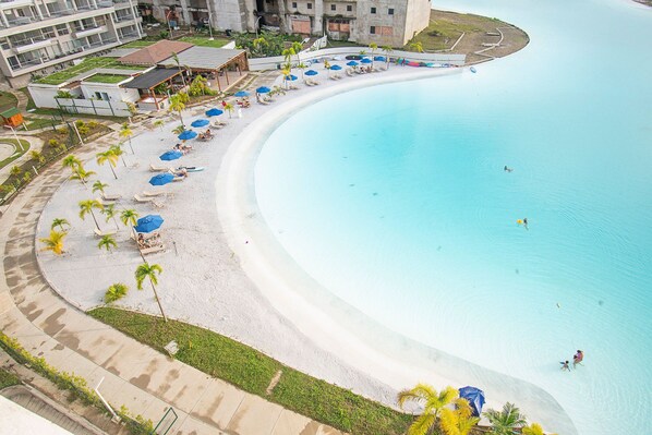 Una playa curvada con piscina, palmeras y sillas de playa.
