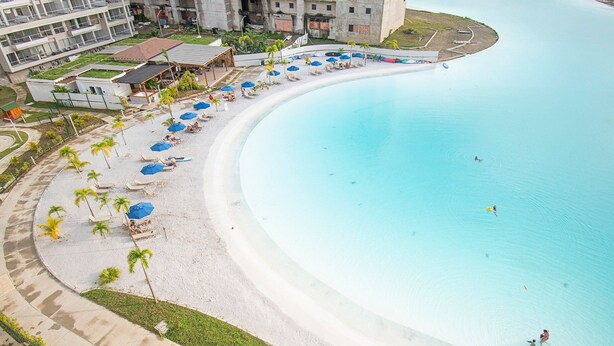 A curved beach with a pool, palm trees, and beach chairs.