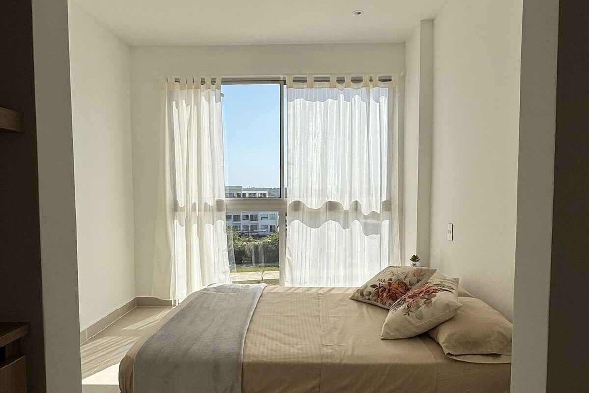 A bedroom with a bed, curtains, a view through the window, and a tiled floor.