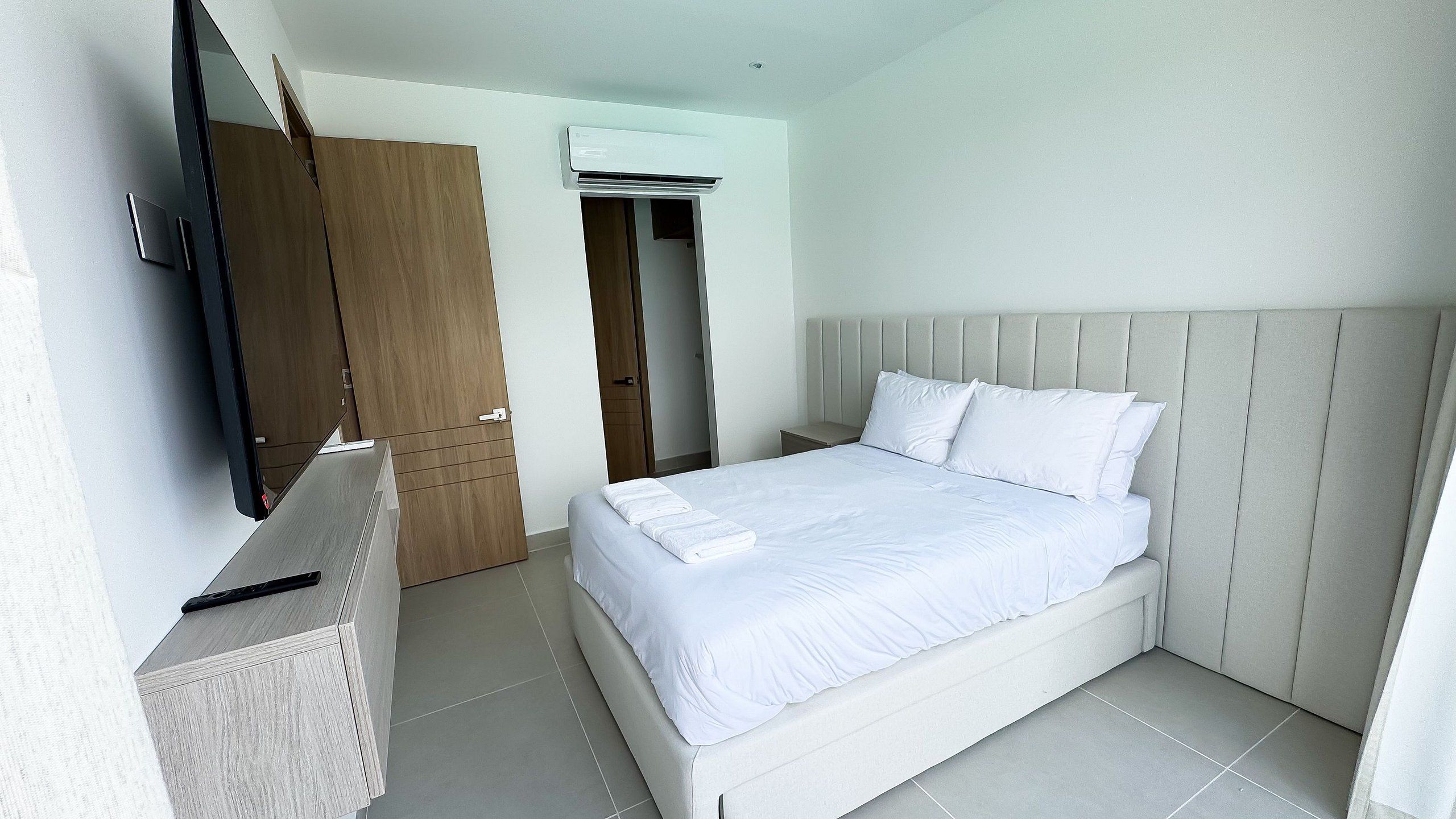 Una habitación de hotel moderna con cama, televisor, armario y aire acondicionado.