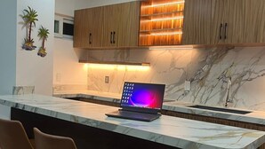 Una cocina moderna con encimera de mármol, armarios de madera, una computadora portátil y taburetes de bar.