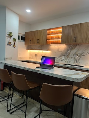 A modern kitchen with a marble countertop, wooden cabinets, a laptop, and bar stools.