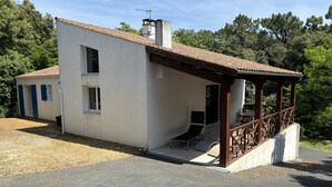 A two-story building with a covered patio area, a small attached structure with blue shutters, and a chimney.