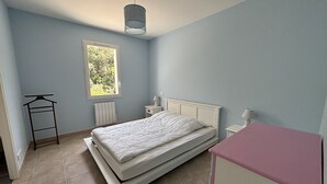 A bedroom with a bed, a window, a radiator, a bedside table, and a hanging clothes rack.