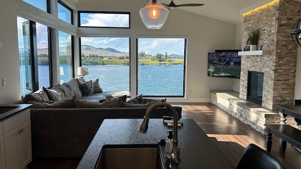 A modern kitchen with a large island, a stone fireplace, and a view of a lake. - New! 3-bedroom lake-front condo on Flathead Lake (Polson)