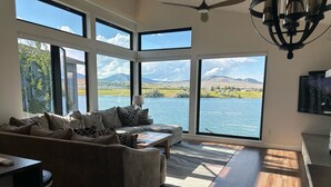 A spacious living room with a large window overlooking a lake and mountains. - New! 3-bedroom lake-front condo on Flathead Lake (Polson)