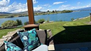 A patio with a view of a lake and mountains, featuring a wicker chair and cushions. - New! 3-bedroom lake-front condo on Flathead Lake (Polson)