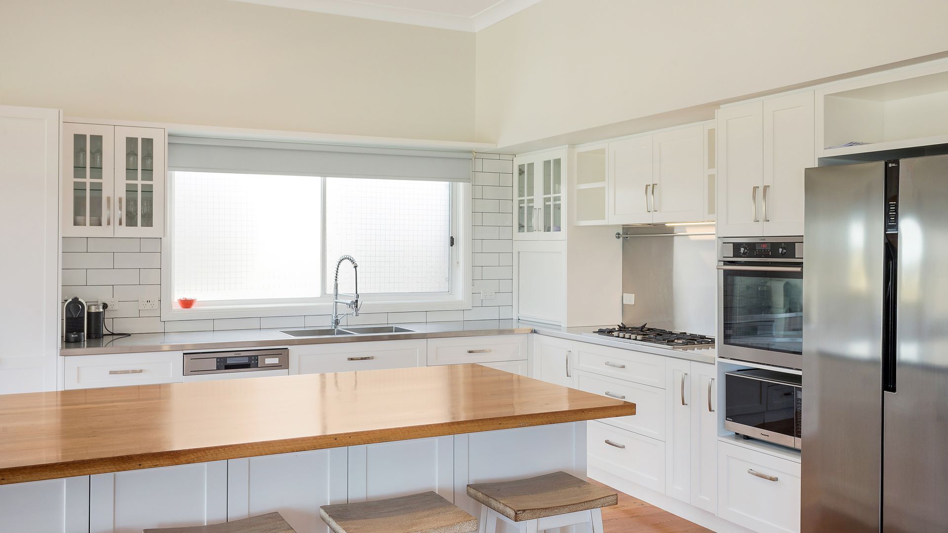 A modern kitchen with white cabinets, a wooden island, stainless steel appliances, and a window with a grid pattern.
