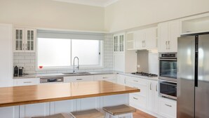 A modern kitchen with white cabinets, a wooden island, stainless steel appliances, and a window with a grid pattern. - 8 Sunnyside Crescent Kianga (Kianga)