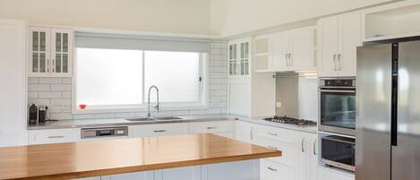 A modern kitchen with white cabinets, a wooden island, stainless steel appliances, and a window with a grid pattern.
