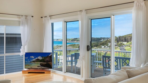 A room with a large sliding glass door leading to a balcony with a view of the ocean and hills. - 8 Sunnyside Crescent Kianga (Kianga)