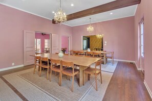 A dining room with a large wooden table and chairs, pink walls, and chandeliers. - Westholme Park (Los Angeles)