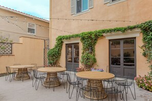 An outdoor patio with round wooden tables and black metal chairs, surrounded by a peach-colored building with a tiled roof and ivy-covered walls. - Westholme Park (Los Angeles)