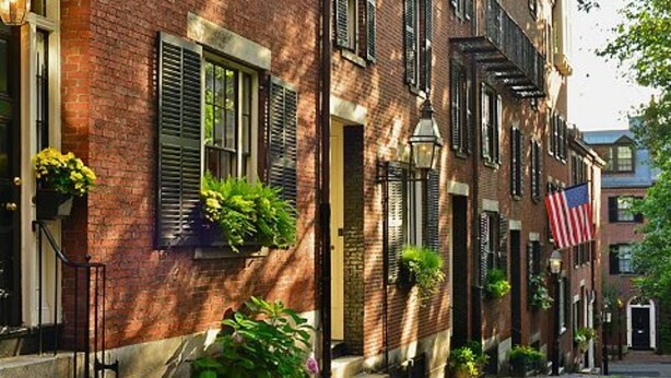 A row of brick townhouses with shutters, a cobblestone street, and an American flag. - Cityscape (Chelsea)