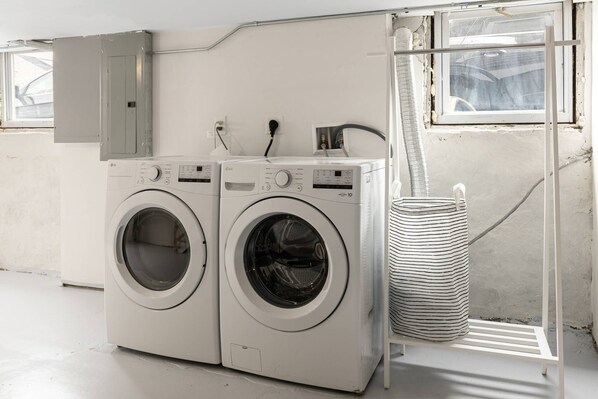 A laundry room with two white front-loading washing machines, a utility cabinet, and a striped laundry basket on a metal rack. - Cityscape (Chelsea)