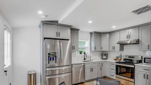 A modern kitchen with grey cabinets, stainless steel appliances, and a dining area with a table set for four. - Cityscape (Chelsea)