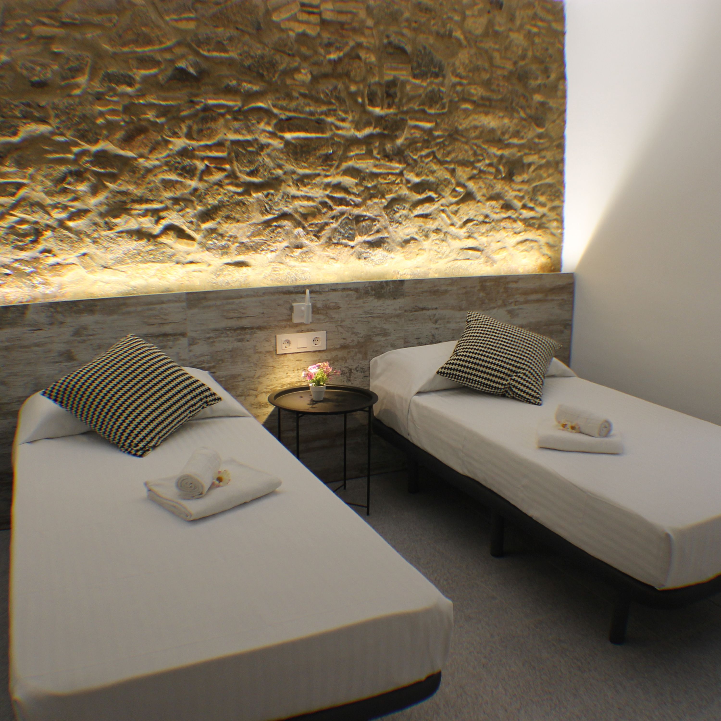 Une chambre d’hôtel avec deux lits simples, une petite table ronde avec une lampe et un mur à texture.