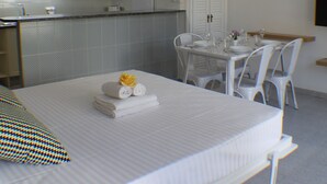 Una habitación de hotel con una cama bien hecha, una mesa de comedor para dos personas y una pequeña cocina.