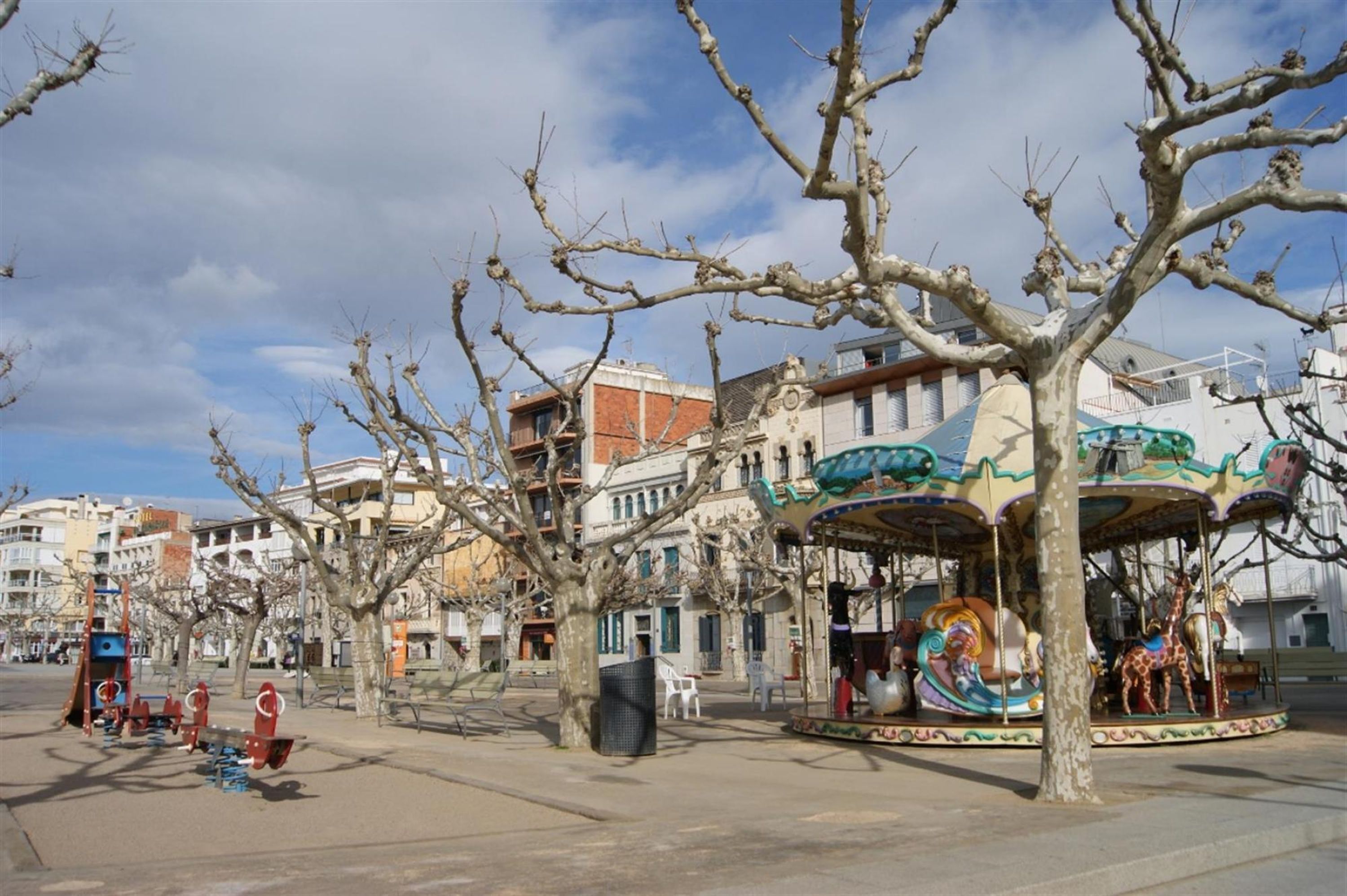 Un carosello in una piazza pubblica, circondato da alberi spogli e edifici.