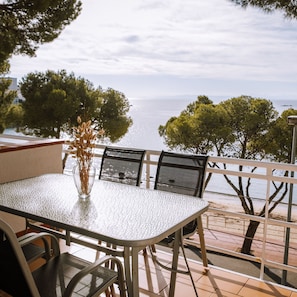 Ein Balkon mit Tisch und Stühlen, mit Blick auf ein Gewässer und Bäume.
