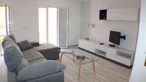 A modern living room with a grey sofa, a glass coffee table, a flat-screen TV, and a sliding glass door leading to a balcony. - Cosconilles 2 in Roses (Roses)