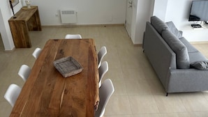 A modern living room with a wooden dining table, white chairs, a grey sofa, and a television. - Cap Llarg 9 in Roses (Roses)
