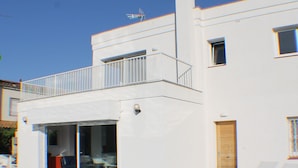 A modern white building with a balcony, a pool, and a door leading to a covered patio area. - Cap Llarg 9 in Roses (Roses)