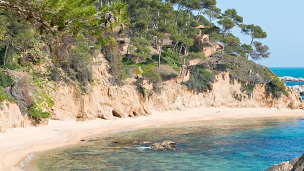 A beach with clear turquoise water, sandy shore, and rocky outcrops. - Cap Llarg 9 in Roses (Roses)