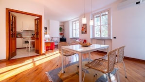 A spacious dining area with a white table and wicker chairs, a kitchen with white cabinets, and a large window providing natural light. - Gerbett Apartment with Terrace by Wonderful Italy (Como)