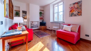 A spacious living room with a red sofa, wooden flooring, a fireplace, and a large window providing natural light. - Gerbett Apartment with Terrace by Wonderful Italy (Como)