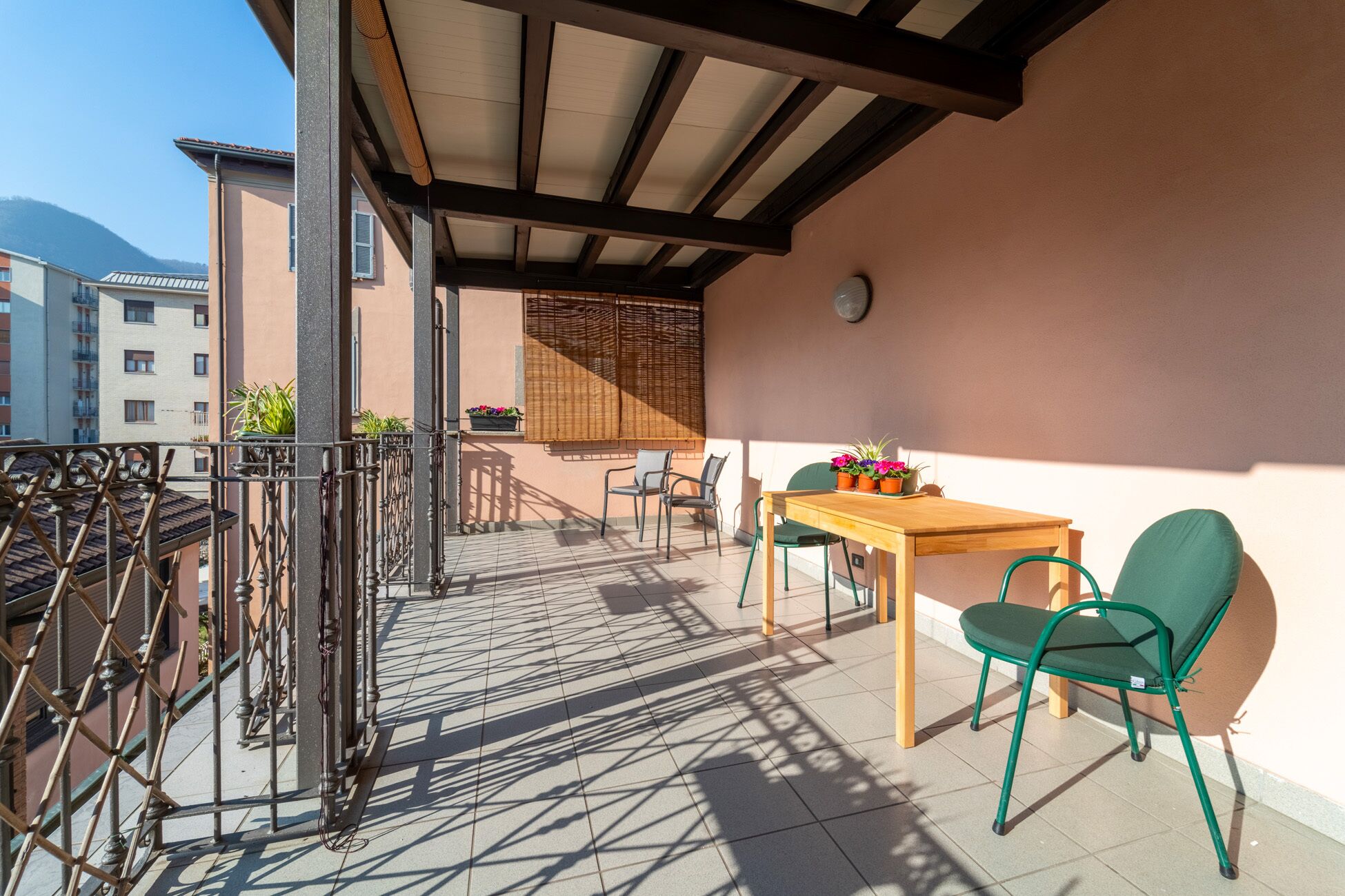 Ein Balkon mit Holztisch und -stühlen, Topfpflanzen und Blick auf Gebäude und Berge.