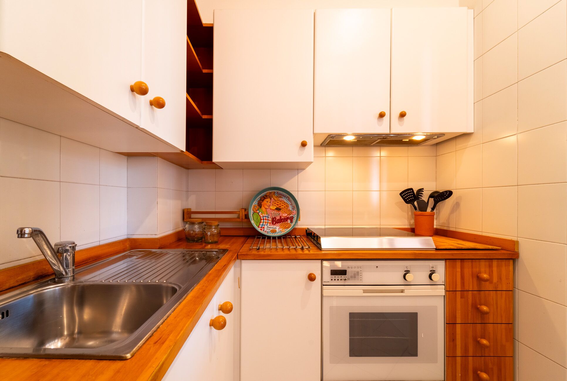 A compact kitchen with white cabinets, a stainless steel sink, a built-in oven, and wooden countertops.