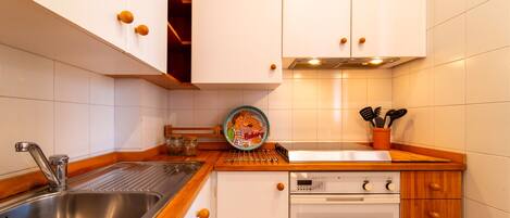 A compact kitchen with white cabinets, a stainless steel sink, a built-in oven, and wooden countertops.