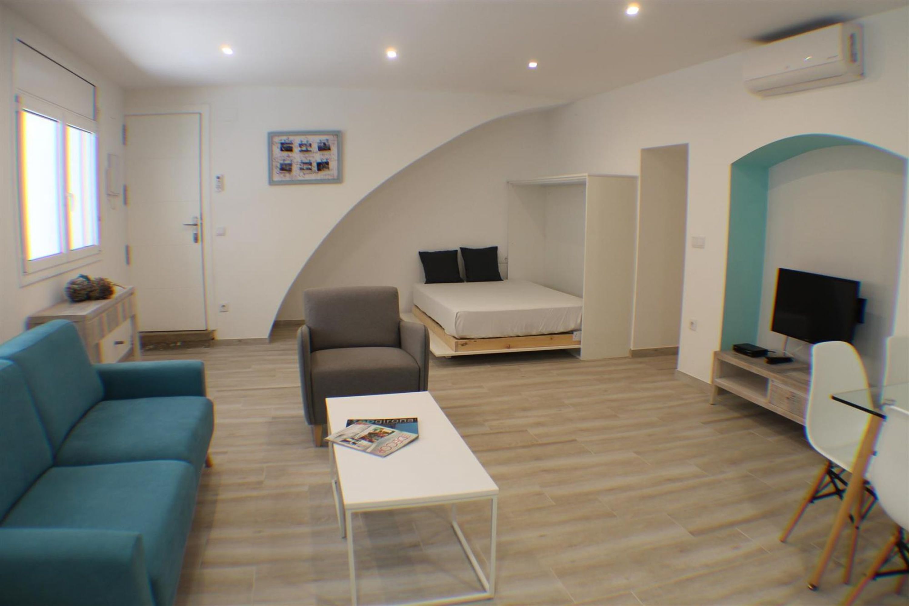 Ein gemütlicher, kleiner Wohnraum mit einer Couch, einem Tisch, einem Bett, einem Fernseher und einem TV-Schrank.