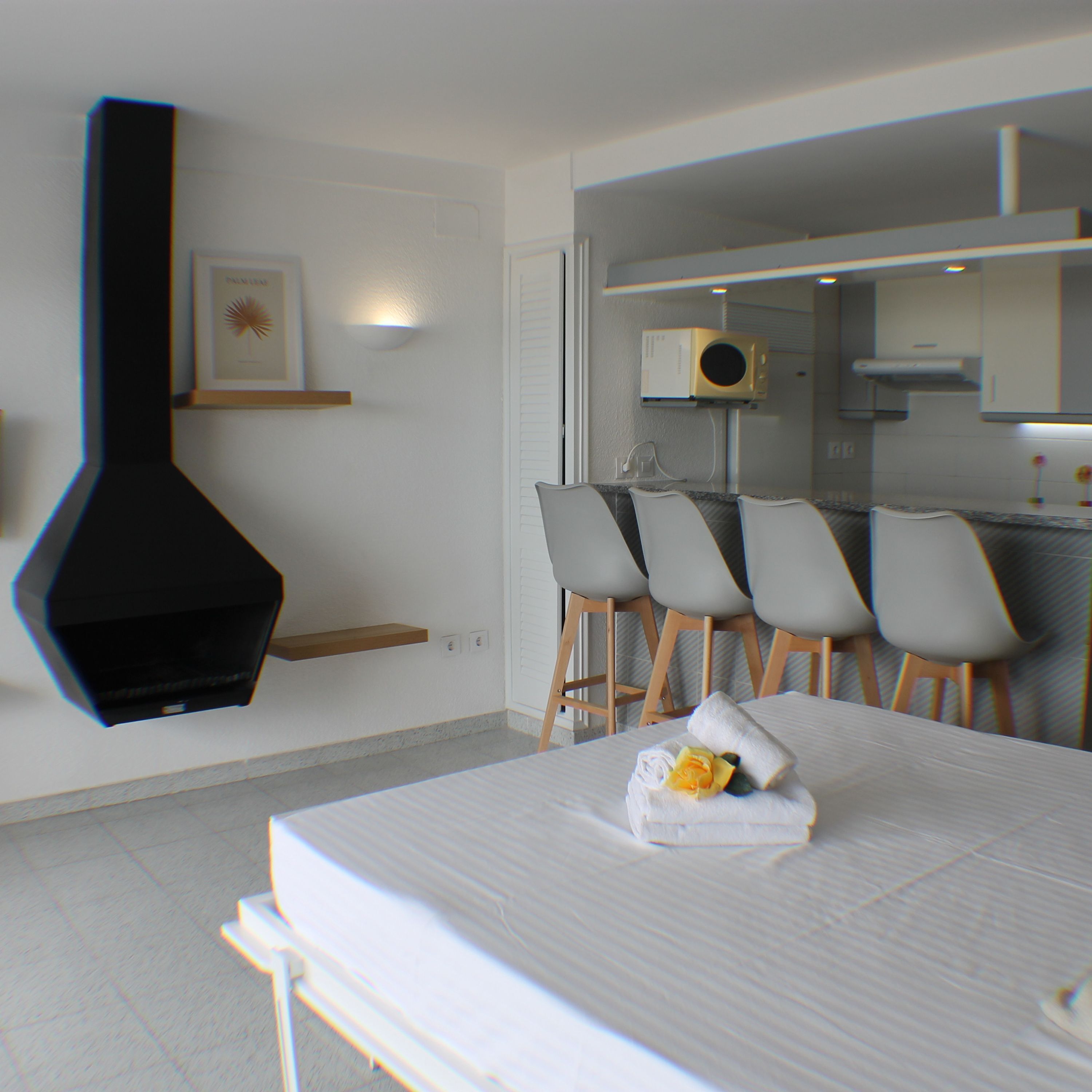 A modern dining area with a long table, multiple chairs, a black kitchen range hood, and a small shelf with a framed picture.