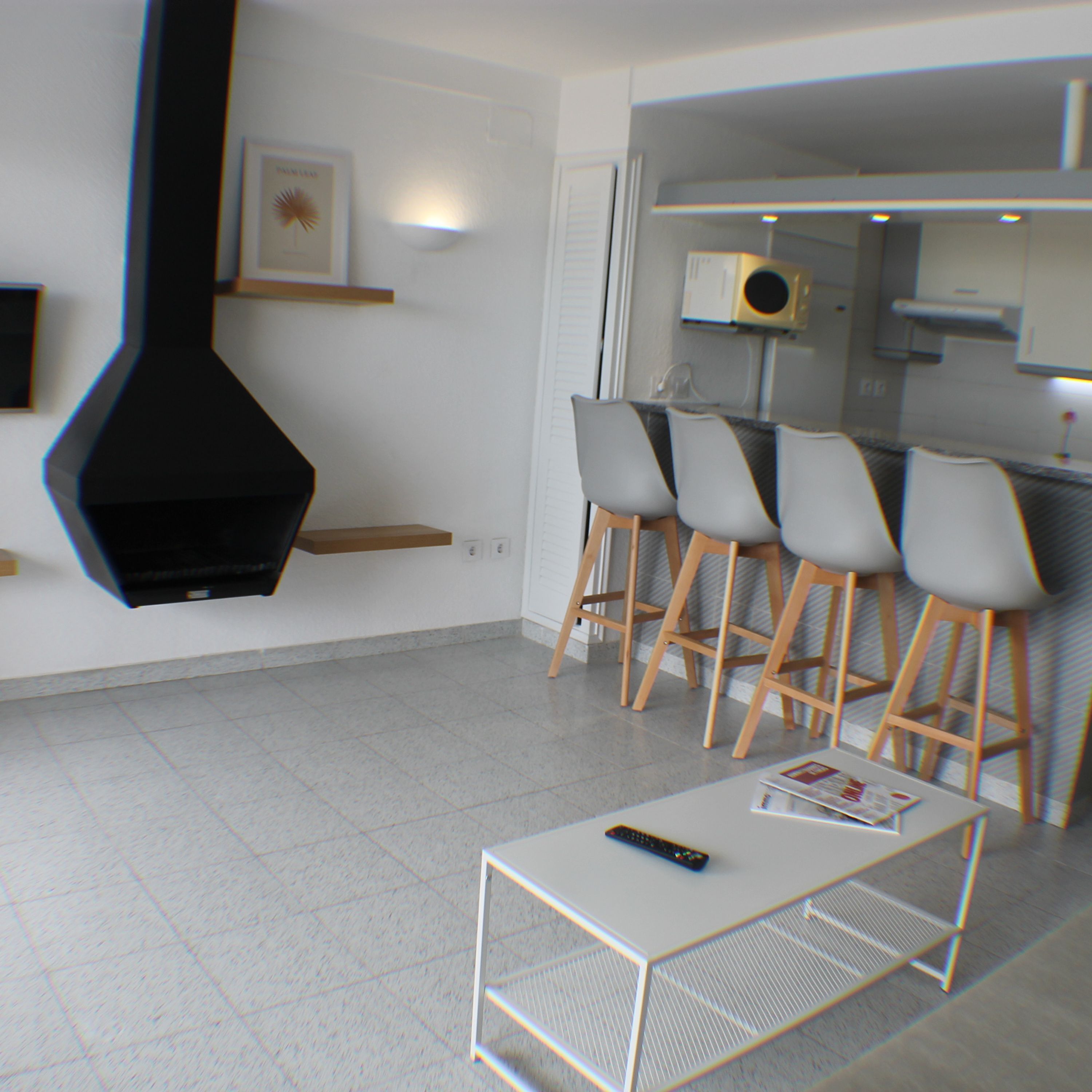 A modern living room with a fireplace, a dining area with bar stools, and a kitchen area with a microwave.