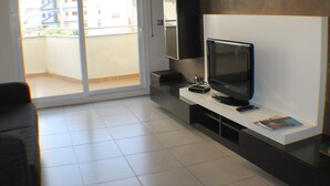 A modern living room with a flat-screen TV, a sofa, and a sliding glass door leading to a balcony. - Drugstore B E in Roses (Roses)